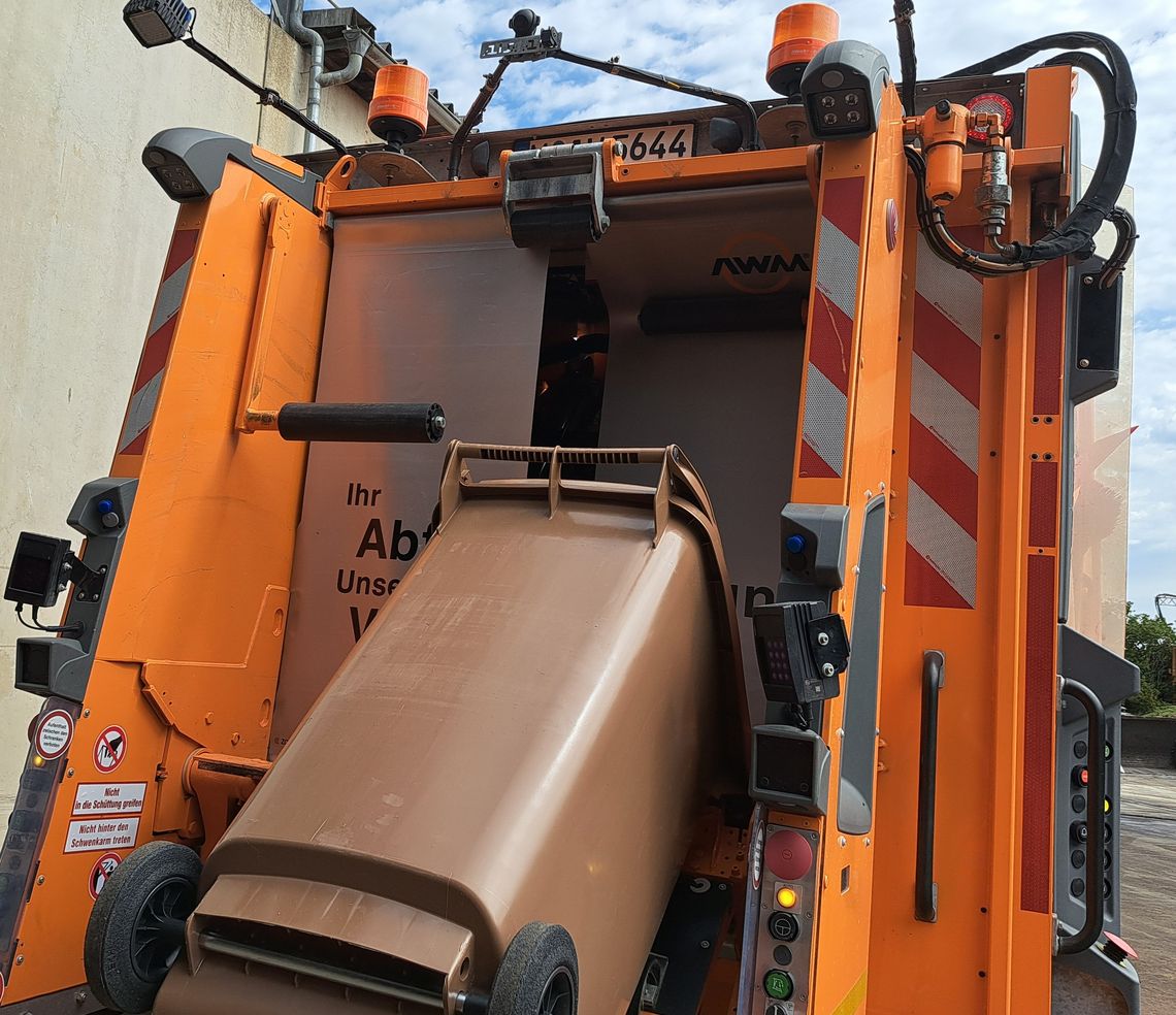 Eine Biomülltonne wird in ein Müllfahrzeug geleert, welches mit Kamera und Sensoren ausgestattet ist. 